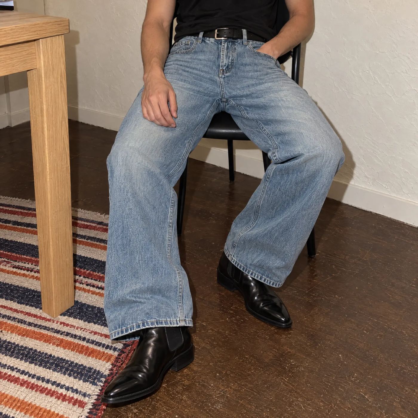 Model seated in light-wash wide-leg jeans with a black belt and boots